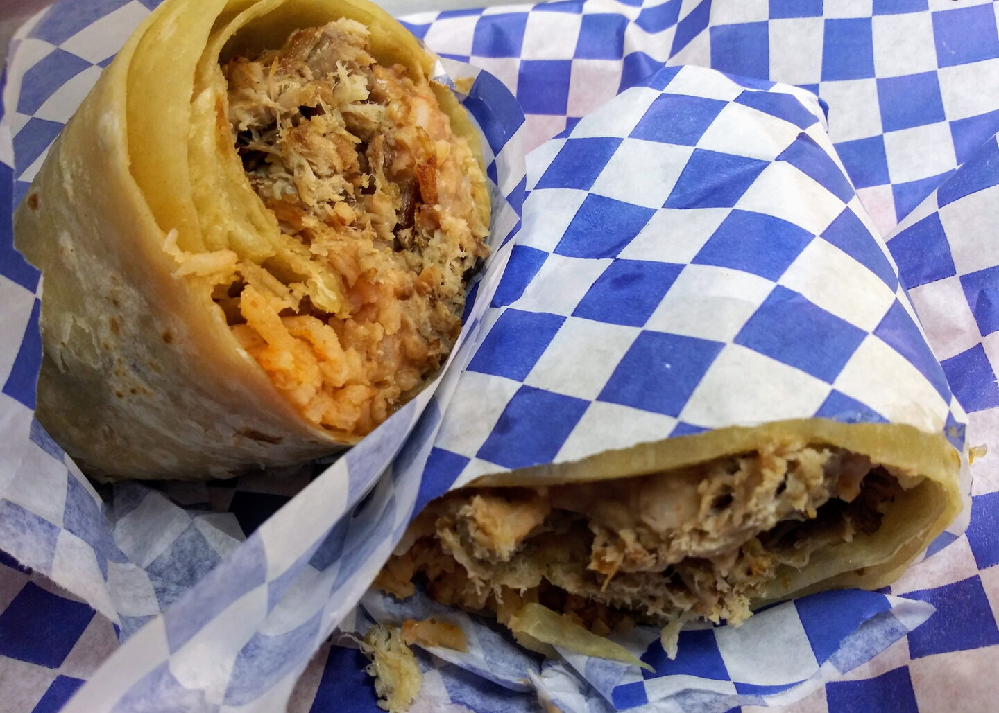 A burrito cut in half, meat, rice and beans inside, wrapped in their blue-and-white checkered paper